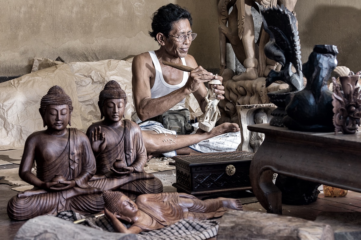 an artisan crafting some statues, wearing a white tank top, featuring several finished Hindu statues