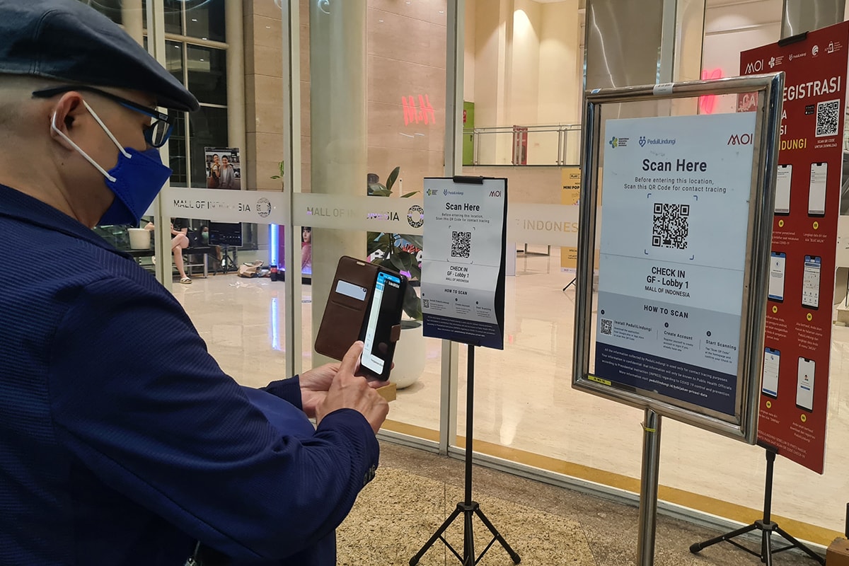 a man checking in on a mall entrance using PeduliLindungi mobile app