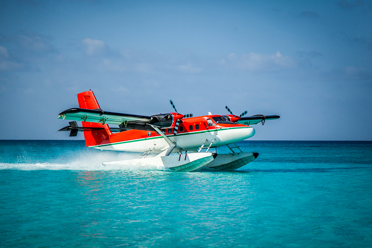 a red-orange and white seaplane takeoff from the ocean