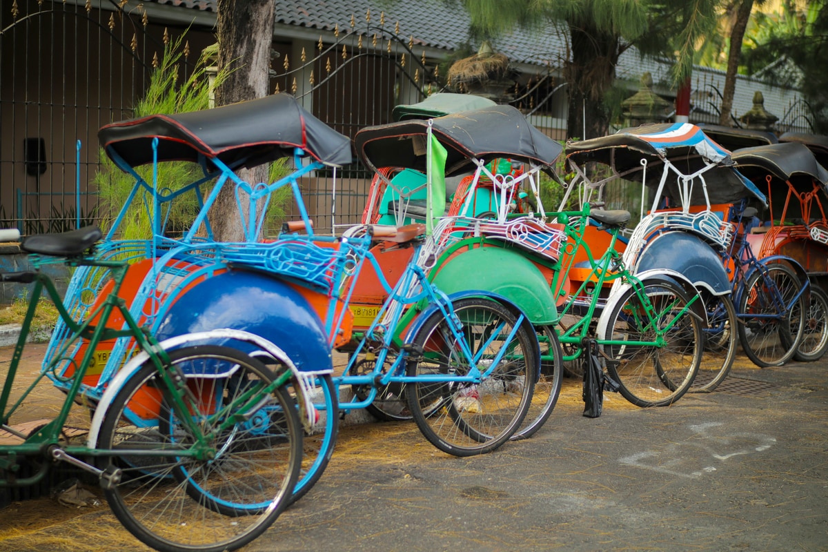 a row of colorful becak parked at the sidewalk in Indonesia
