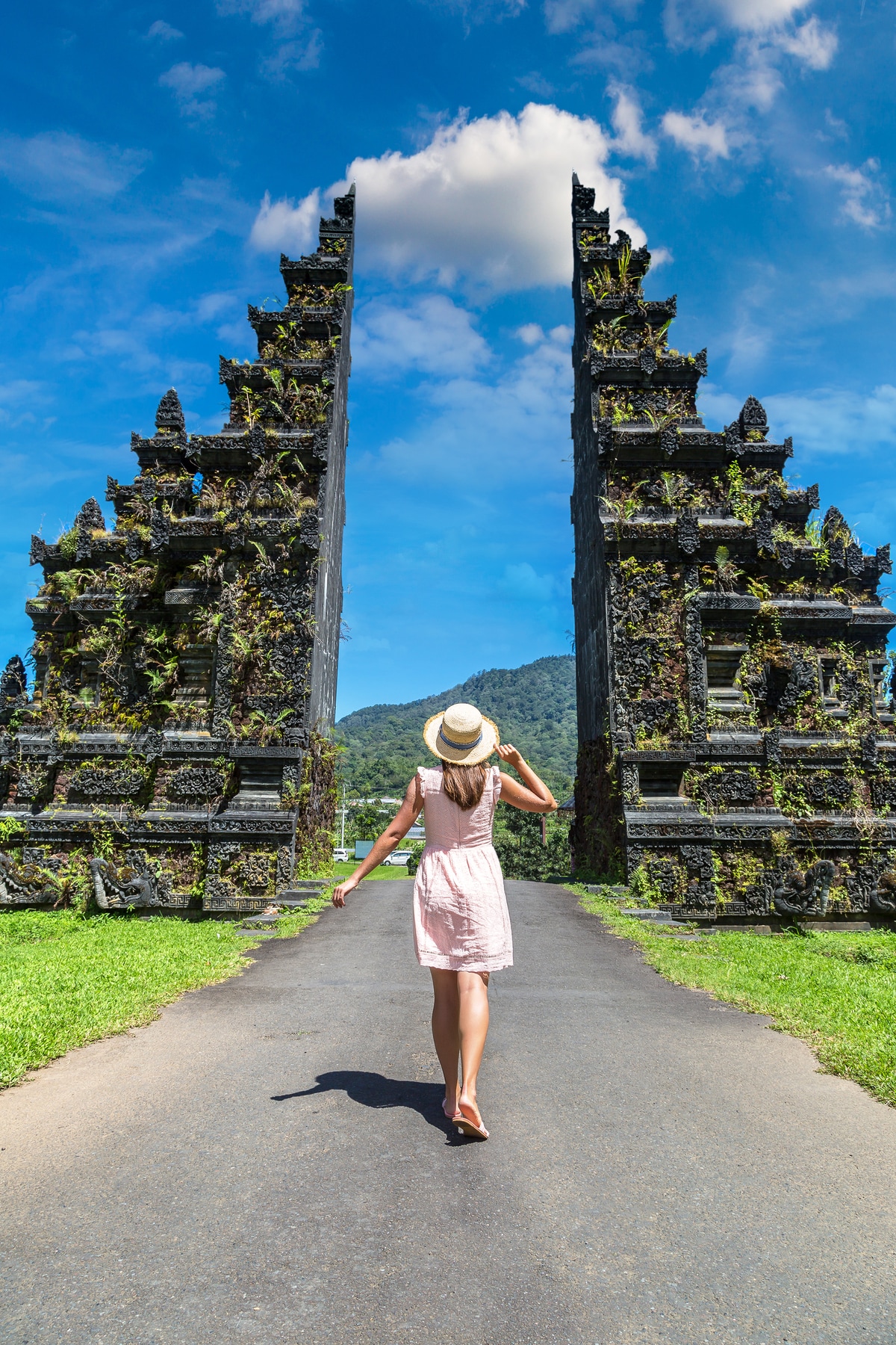 a woman wearing a dress and hat backposing between a gate