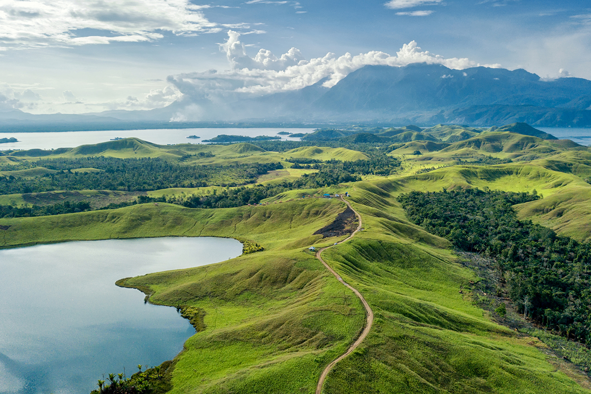 Danau di sela-sela perbukitan, jalan melengkung-lengkung di perbukitan, air danau yang merefleksikan langit, bentuk danau seperti amoeba