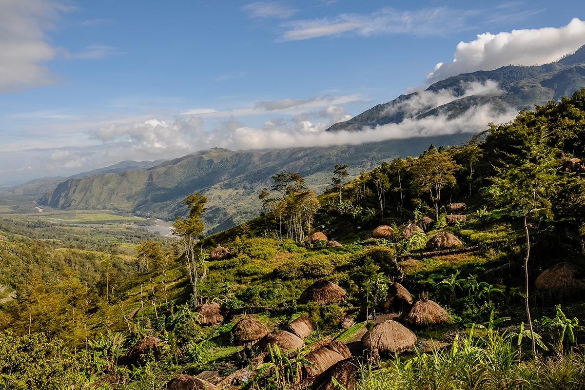 Deretan Honai, rumah tradisional Papua di Lembah Baliem, pedesaan asri di kaki gunung Jayawijaya, langit biru cerah serta awan yang menghampiri pegunungan