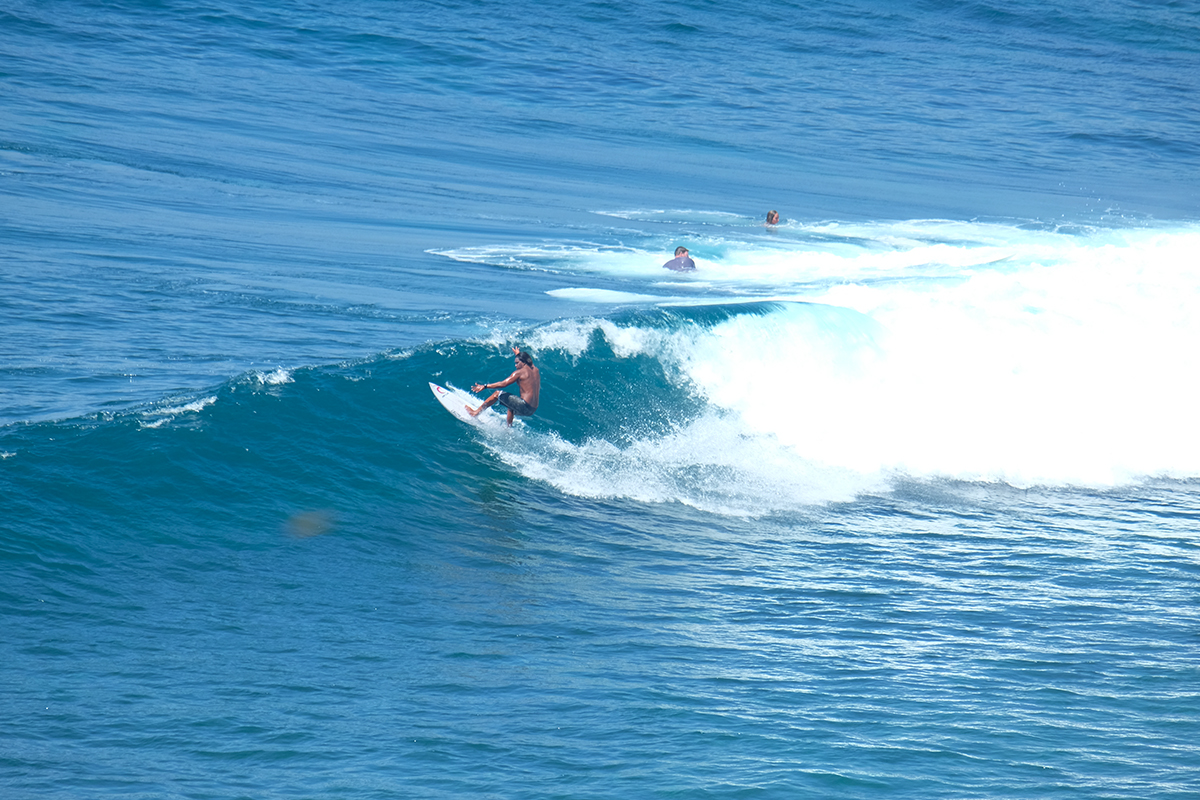 Potret laki-laki sedang berselancar di gulungan ombak