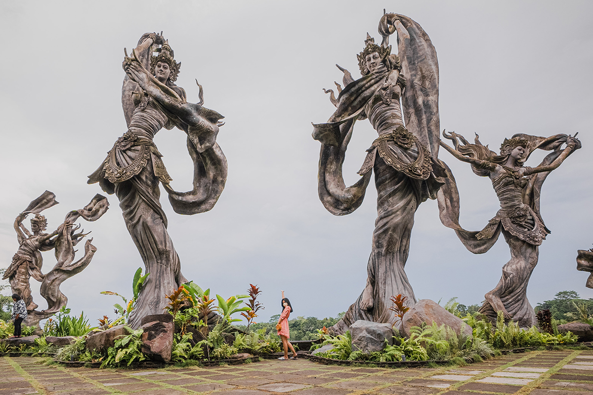 Seorang wanita berdiri di tengah patung-patung raksasa Taman Dedari